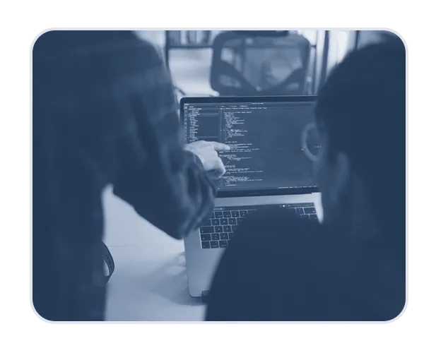 close crop photo of person sitting at laptop and with another person stnaind over their left shoulder pointing at screen